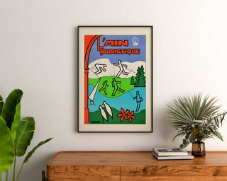 Vintage-Reiseplakat – L’Ain touristique, gerahmt über einer Holzkommode zwischen Pflanzen.