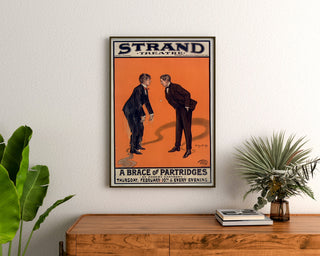 Manifesto vintage A Brace of Partridges, Strand Theatre, incorniciato sopra una cassettiera in legno, tra piante.