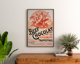 Manifesto vintage Beef Chocolat, cioccolateria della Drôme, incorniciato sopra una cassettiera in legno, tra piante.