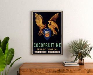Manifesto vintage Cocofruitine, burro vegetale, incorniciato sopra una cassettiera in legno, tra piante.