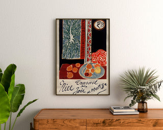Vintage-Poster "Nice, Arbeit und Freude", gerahmt über einer Holzkommode, zwischen Pflanzen.