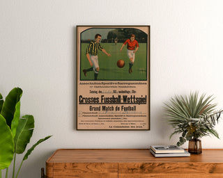 Manifesto vintage Sarreguemines, partita di calcio, incorniciato sopra una credenza in legno, tra delle piante.